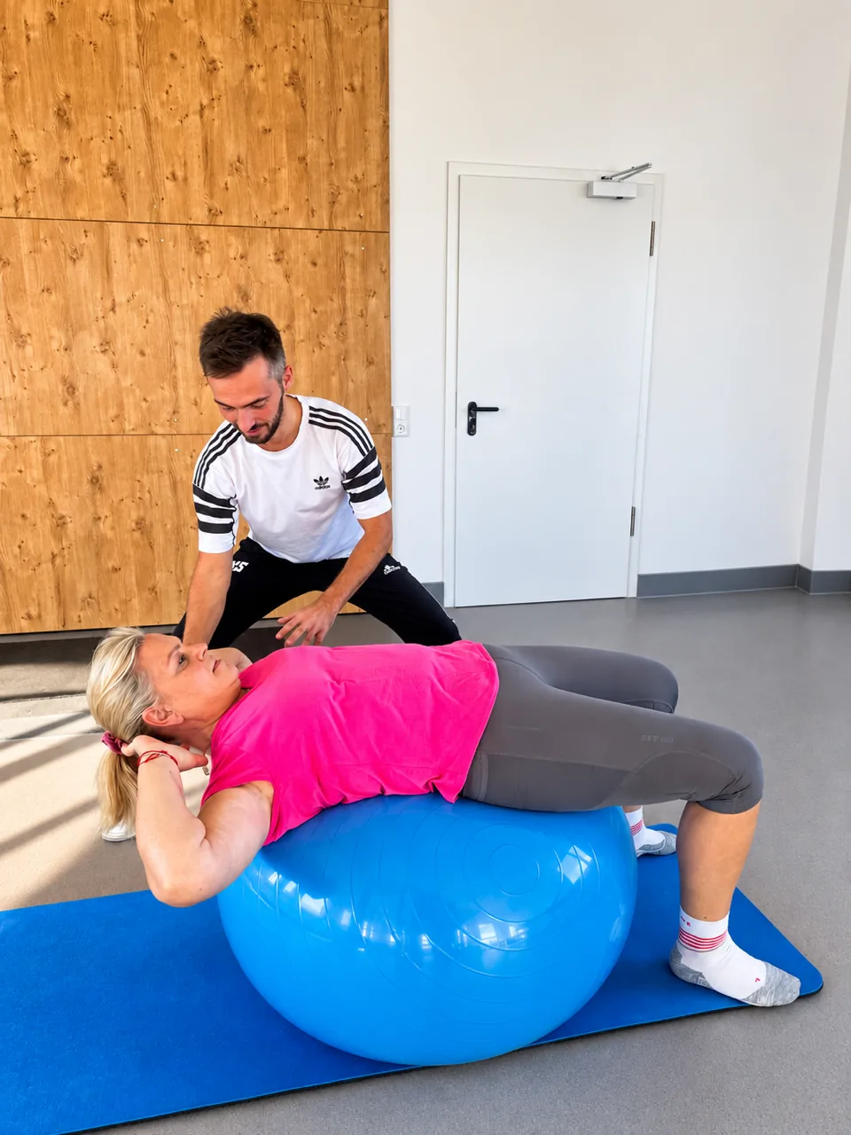 Eine Teilnehmerin dehnt sich rücklings über dem Gymnastikball, Nils sichert den Ball